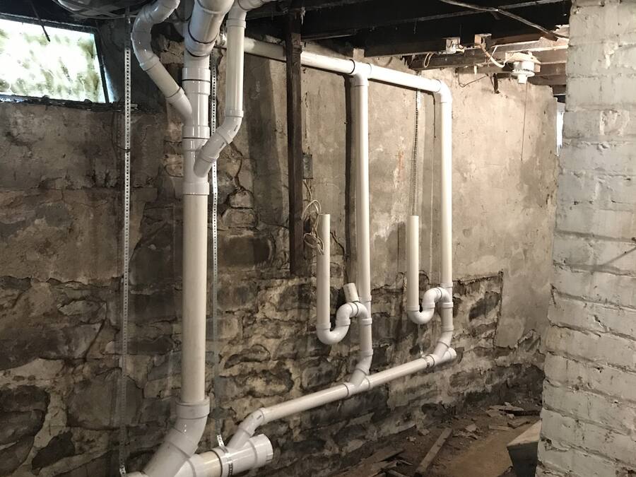 Replacement PVC drain stack and branch lines on a stone foundation wall