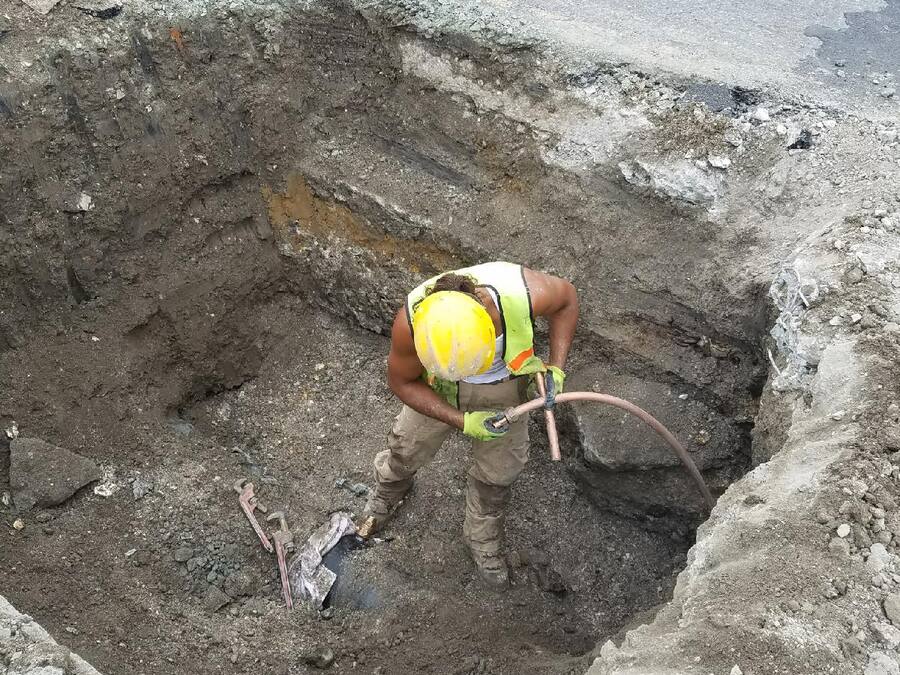 Heavy Duty Plumbing technician replacing a water service line in a street excavation