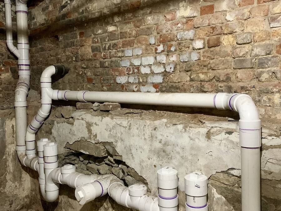 New PVC waste and vent piping installed along a basement brick wall